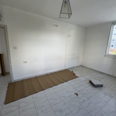 חדר עם קיר לבן וקרטון על הרצפה, מוכן לצביעה