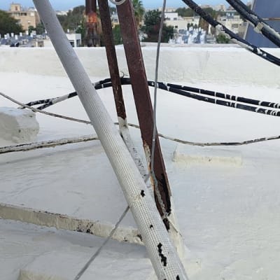 גג אטום עם חומר לבן, כבלים וברזלים חלודים