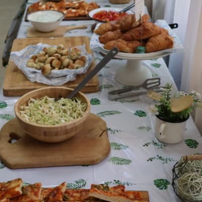 מגוון מאכלים על שולחן קייטרינג, כולל פיצות, סלטים וקוראסונים.