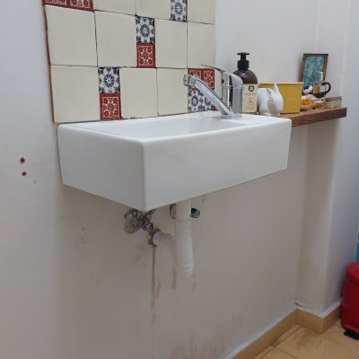 כיור עם ברז, אריחים צבעוניים, ומדף עם חפצים שונים