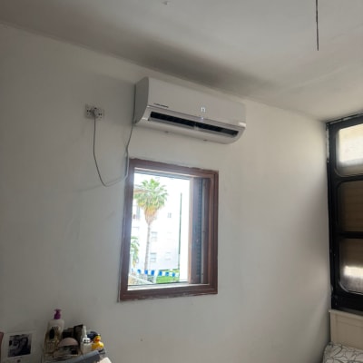 מזגן מותקן על קיר לבן מעל חלון פתוח