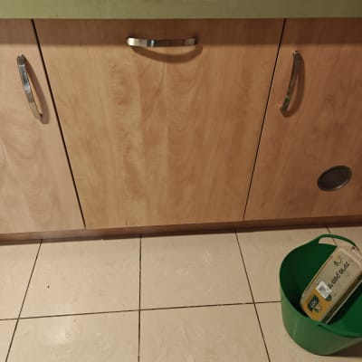 ארון מטבח עם ידיות מתכת ודלי ירוק על הרצפה