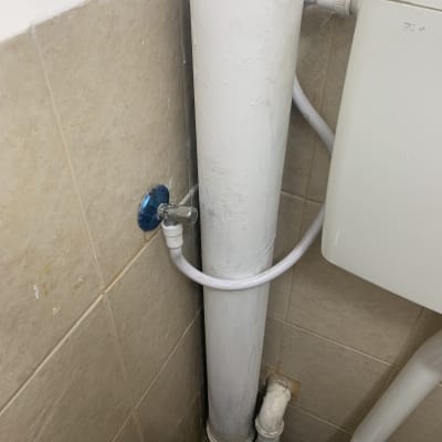 צינור מים לבן עם ברז כחול על קיר אריחים