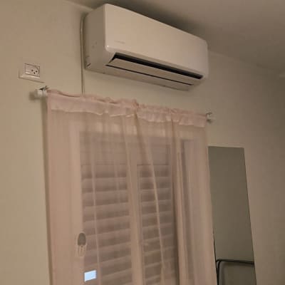 מזגן קיר לבן מותקן מעל חלון עם וילון