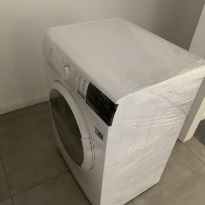 מכונת כביסה עטופה בניילון על רצפה אפורה