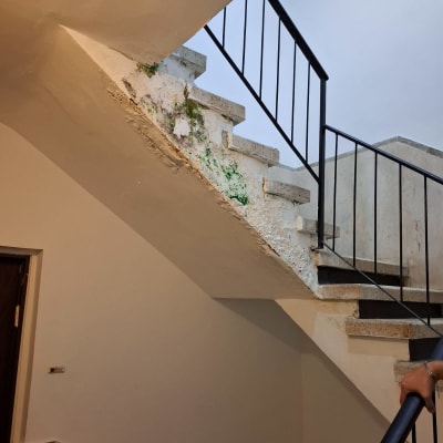 מדרגות עם סימני רטיבות וקילוף צבע, מעקה מתכת שחור.