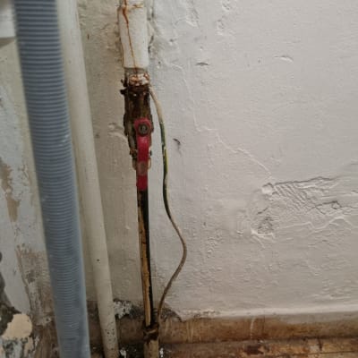 צינור חלוד עם ברז אדום על קיר לבן