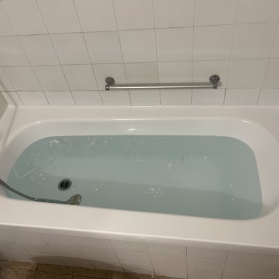 אמבטיה עם מים, אריחים לבנים ומעקה מתכת