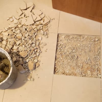 רצפה עם אריחים שבורים ודלי עם מלט