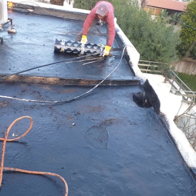 אדם מיישם יריעות איטום על גג שטוח