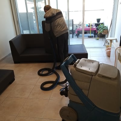 אדם מנקה ספה עם מכונת ניקוי מקצועית