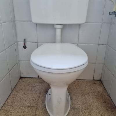 אסלה לבנה עם צינור מים מחובר לקיר