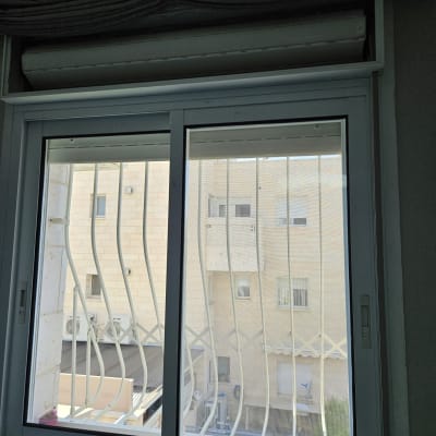 תריס גלילה סגור מעל חלון זכוכית עם סורגים