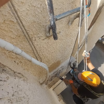 אדם עם קסדה צובע קיר חיצוני בעזרת חבלים