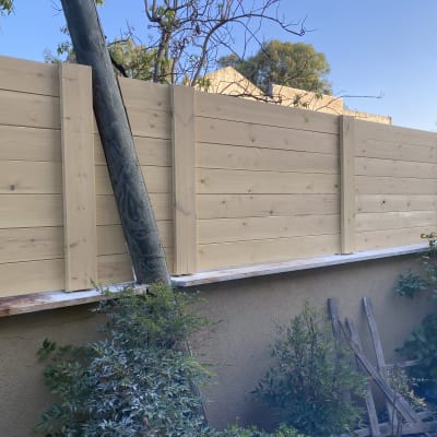 גדר עץ בהירה עם עמוד עץ וגינה קטנה