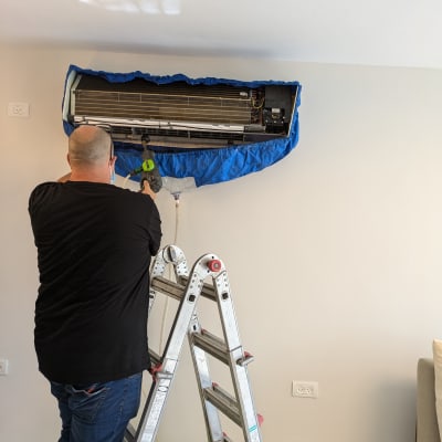 טכנאי על סולם מנקה מזגן עם שואב אבק