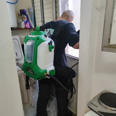 מדביר עם מיכל ריסוס ירוק על הגב בחדר קטן