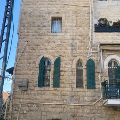 קיר אבן עם חלונות ותריסים ירוקים, סולם וחפצים על הקיר