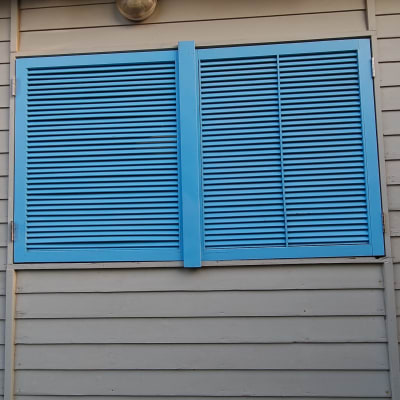 תריסי עץ כחולים מותקנים על קיר עץ אפור