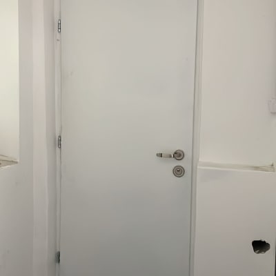 דלת לבנה עם ידית מתכת, קירות מסוידים וצנרת חשופה בתחתית