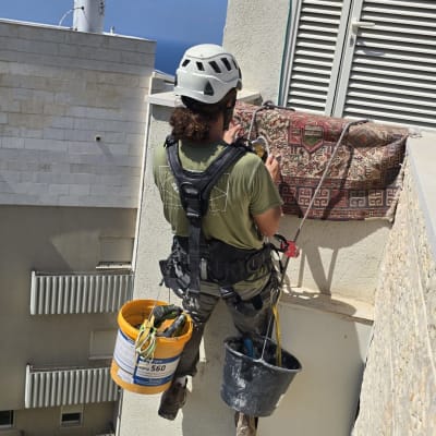 עובד בגובה עם קסדה וציוד בטיחות על קיר בניין