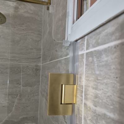 דלת מקלחת זכוכית עם ציר זהב על קיר שיש