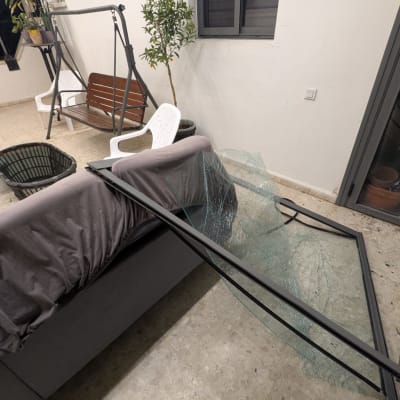 זכוכית שבורה על רצפה ליד ספה מכוסה בבד אפור