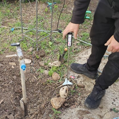 אדם בודק דליפת מים בגינה עם מכשיר מדידה