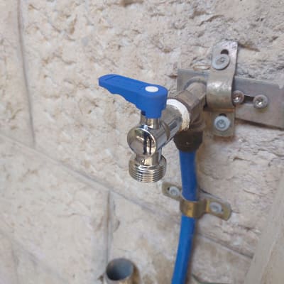 ברז מים עם ידית כחולה על קיר אבן