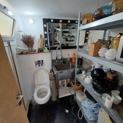 חדר עם כיור נירוסטה, מדפים מתכתיים וכלי עבודה שונים.