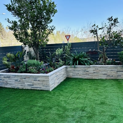 גינה עם דשא מלאכותי, ערוגות פרחים ועצים קטנים