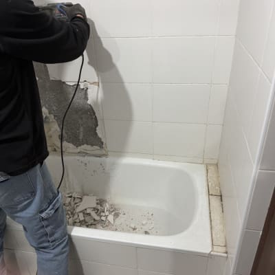 אדם מסיר אריחים עם כלי חשמלי באמבטיה