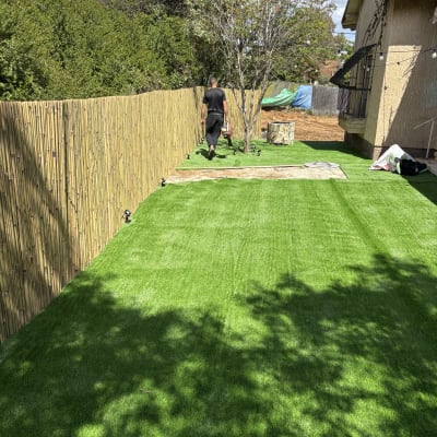 דשא סינתטי עם גדר במבוק ועץ בגינה