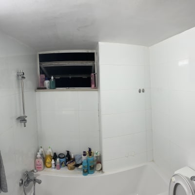 חדר אמבטיה עם אריחים לבנים ומוצרי ניקוי על אדן החלון