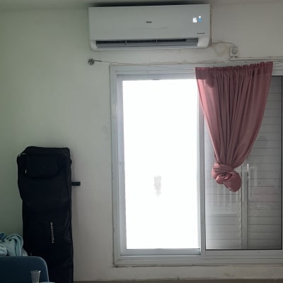 מזגן מותקן על קיר מעל חלון עם וילון ורוד