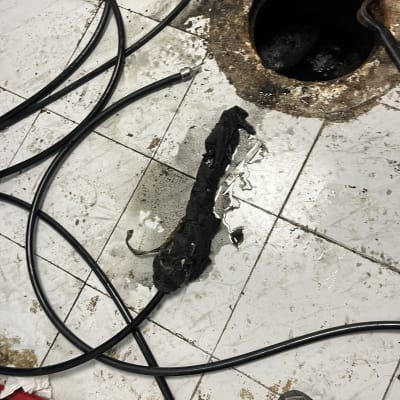 צינור שחור ליד פתח ביוב על רצפה מלוכלכת