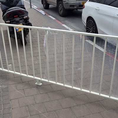 גדר מתכת לבנה על מדרכה ליד מכוניות חונות