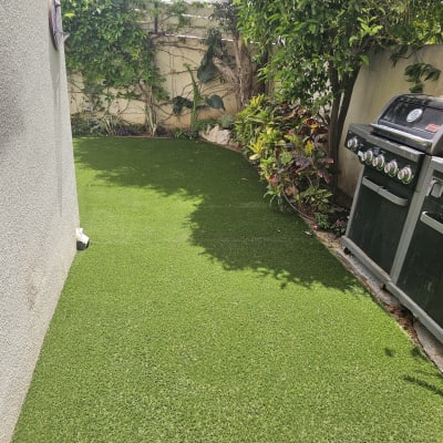 דשא סינטטי עם צמחייה וגריל גז בגינה