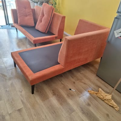 ספות כתומות עם כריות על רצפת עץ, כלי ניקוי ליד