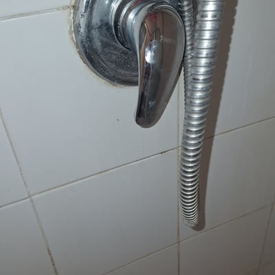 ברז מקלחת עם צינור מתכת על קיר אריחים