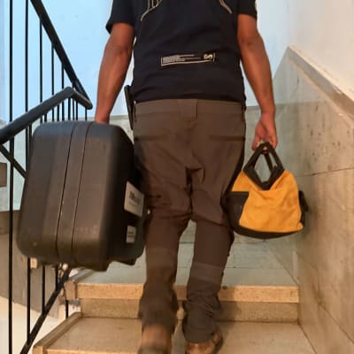 אינסטלטור עולה במדרגות הבניין עם ארגז ותיק כלים