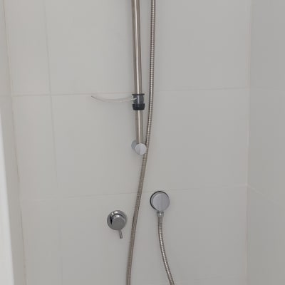 ראש מקלחת חדש עם צינור מתכת על קיר לבן