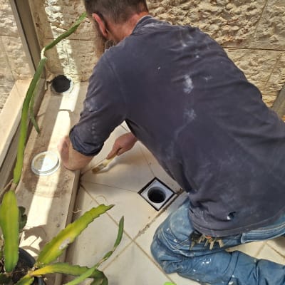 אדם מורח חומר איטום על רצפה ליד צינור פתוח