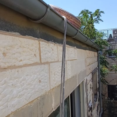 קיר אבן עם צינור ומרזב על גג בניין