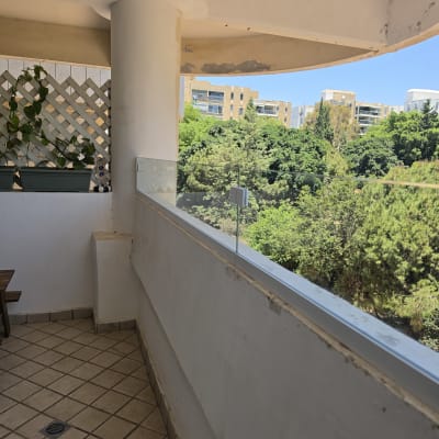 מרפסת עם מעקה זכוכית ונוף לעצים ובניינים
