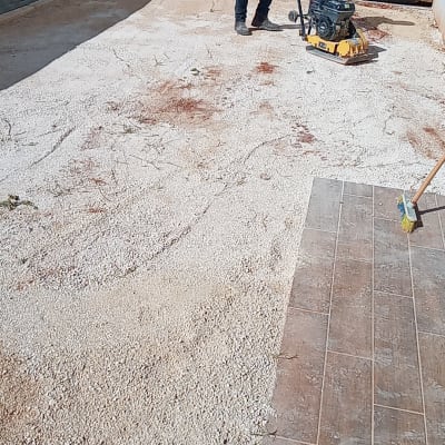 אדם מפעיל מכבש על חצץ בחצר במהלך שיפוץ