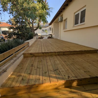 דק עץ בחצר עם עצים ובית ברקע