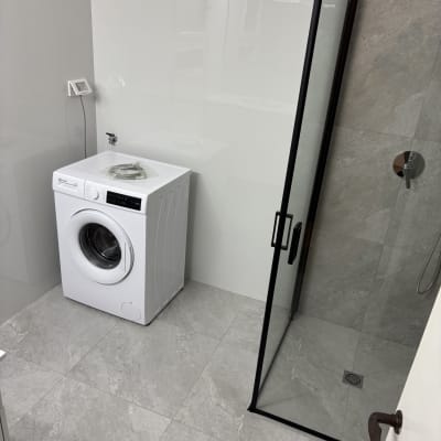 מכונת כביסה בחדר אמבטיה עם מקלחון זכוכית