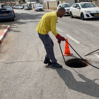 אדם עם צינור ליד פתח ביוב ברחוב