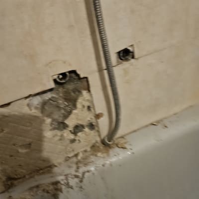 צינור מתכת ליד קיר עם אריחים שבורים